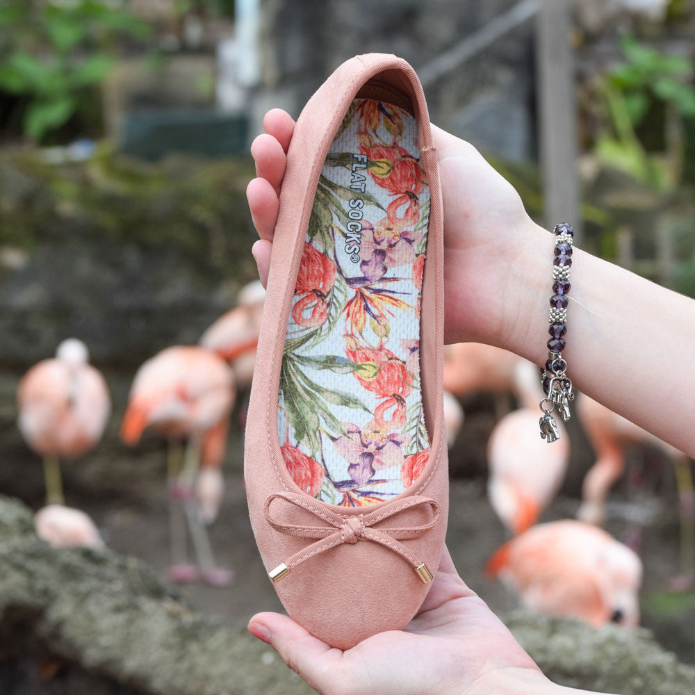 Woman holding up coral flat slip on shoe with Flamazing FLAT SOCKS inside, flamingos in background #size_small-up-to-women-s-11-men-s-10