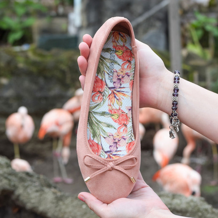 Woman holding up coral flat slip on shoe with Flamazing FLAT SOCKS inside, flamingos in background #size_small-up-to-women-s-11-men-s-10