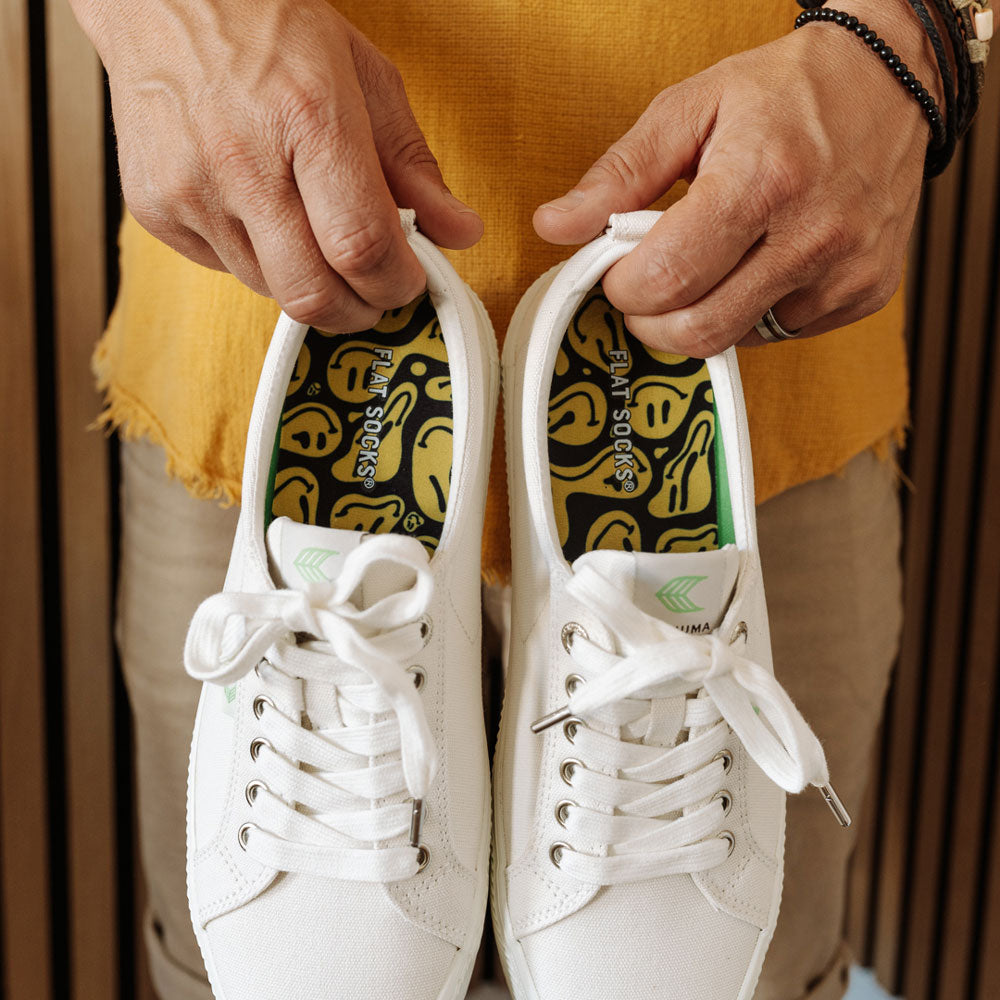 Man holding up white canvas shoes with Happy Days FLAT SOCKS inside #size_large-up-to-women-s-13-men-s-14
