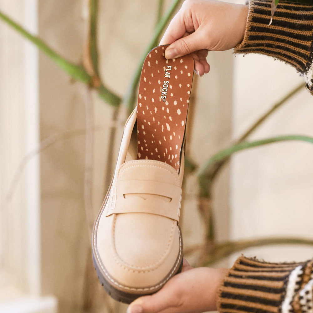 Beige loafer shoe with spotted Fawntastic FLAT SOCKS inside, held by a hand against a blurred natural background #size_small-up-to-women-s-11-men-s-10