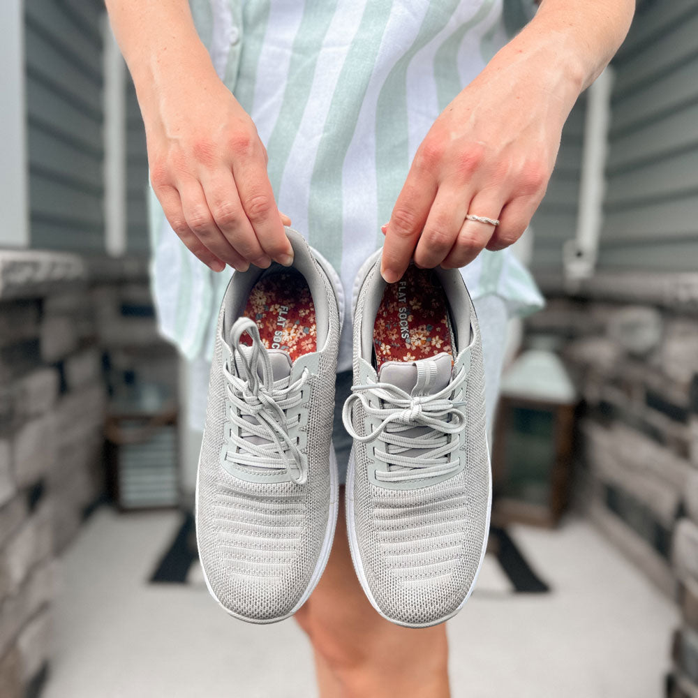 Woman holding up a pair of gray sneakers with Becky Thatcher FLAT SOCKS inside #size_small-up-to-women-s-11-men-s-10