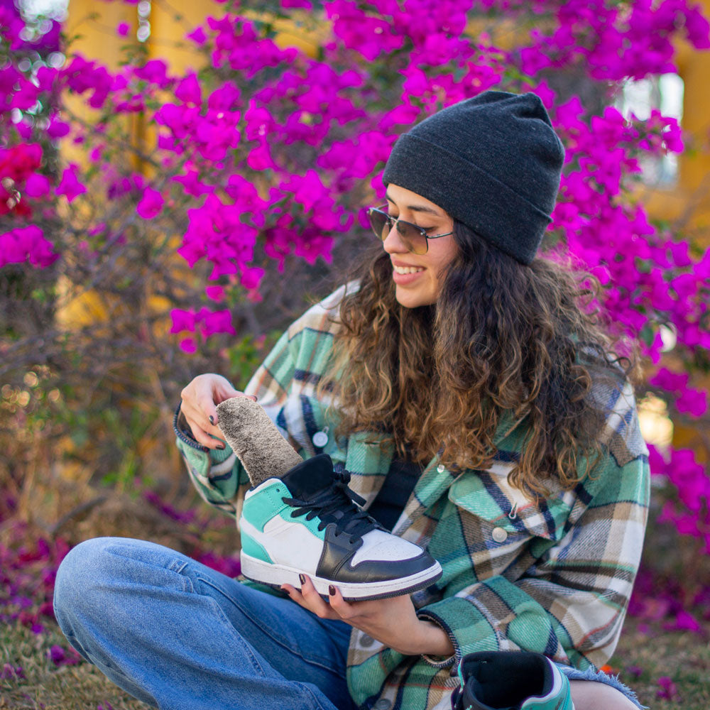 Girl sitting in front of bright pink bush wearing dark gray beanie and flannel shacket while placing Chestnut Faux Fur FLAT SOCKS into sneaker #size_small-up-to-women-s-11-men-s-10