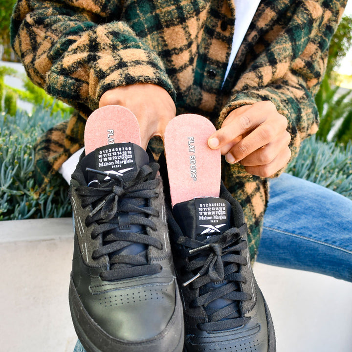 Man sitting outside wearing sherpa shacket while holding up a pair of black sneakers with Colorado FLAT SOCKS inside #size_large-up-to-women-s-13-men-s-14