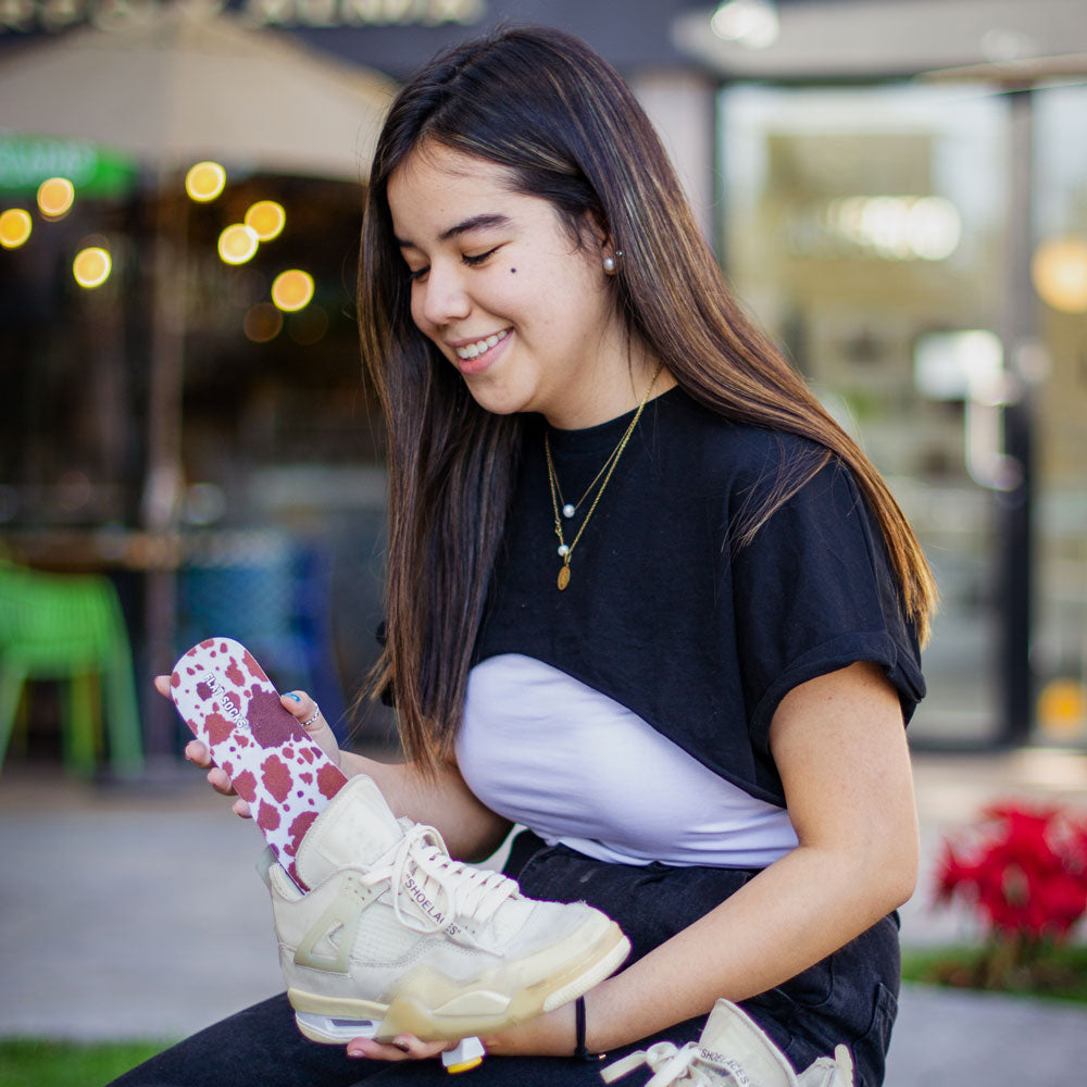 Girl placing Brown Cow Print FLAT SOCKS into tan sneakers #size_large-up-to-women-s-13-men-s-14