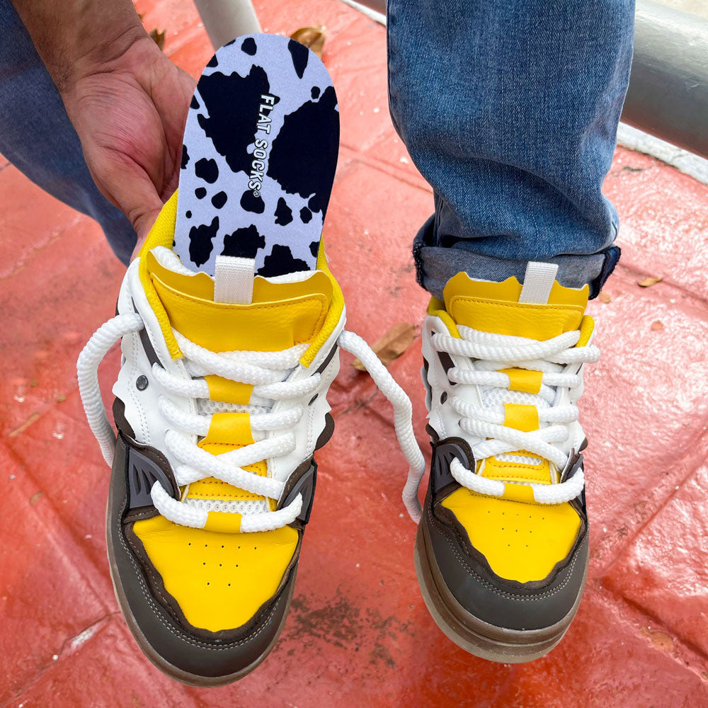 Man showing Black Cow Print FLAT SOCKS in yellow sneaker  #size_large-up-to-women-s-13-men-s-14