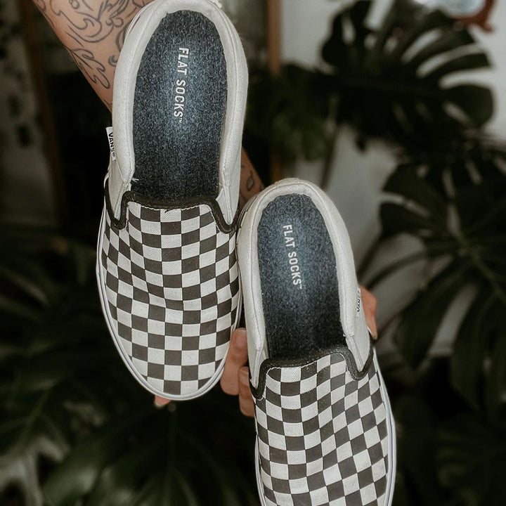 Person holding a pair of checkered Vans shoes with Dark Heather Gray FLAT SOCKS inside #size_small-up-to-women-s-11-men-s-10