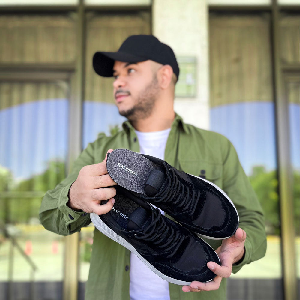 Man standing outside holding a pair of black sneakers with Dark Heather Gray FLAT SOCKS inside #size_large-up-to-women-s-13-men-s-14