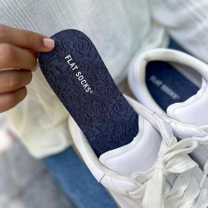 Person placing a pair of Dark Lace FLAT SOCKS into white sneakers #size_large-up-to-women-s-13-men-s-14