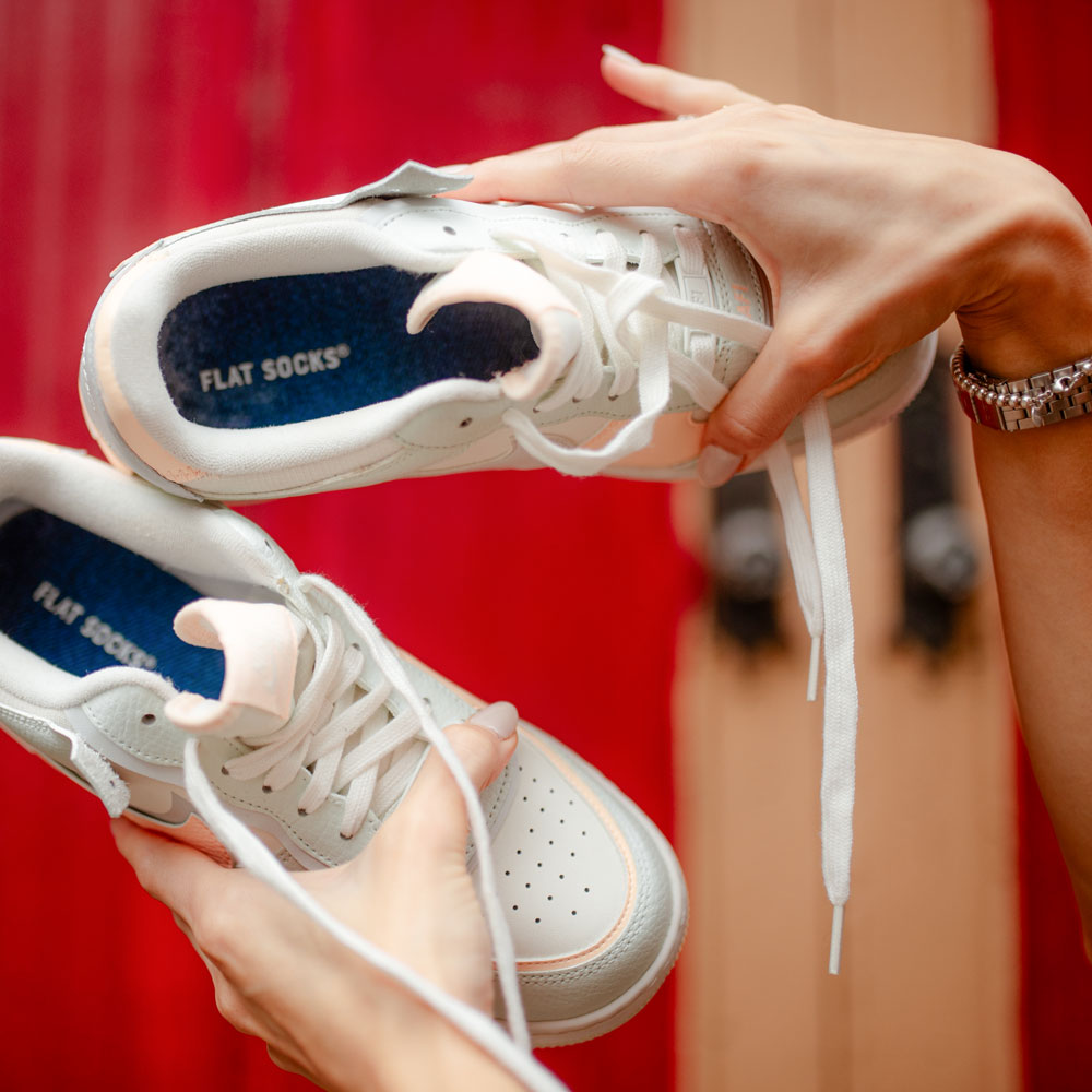 Woman holding up a pair of white shoes with Dominant Jean FLAT SOCKS inside #size_small-up-to-women-s-11-men-s-10