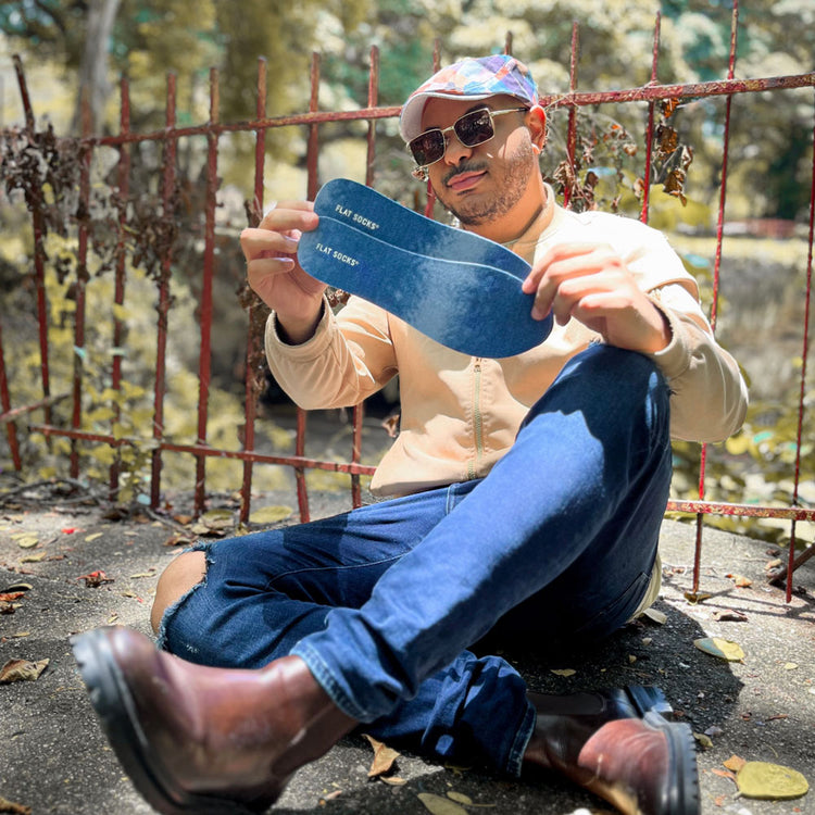 Man sitting in front of rusted gate holding up a pair of Dominant Jean FLAT SOCKS #size_large-up-to-women-s-13-men-s-14