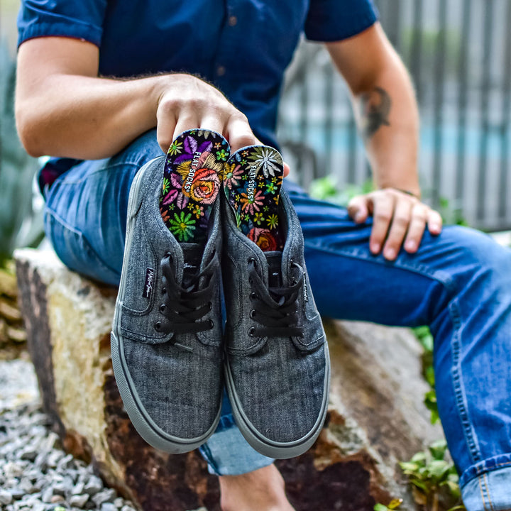 Man sitting outside on a rock while holding a pair of gray sneakers with Floral Embroidery FLAT SOCKS inside #size_large-up-to-women-s-13-men-s-14