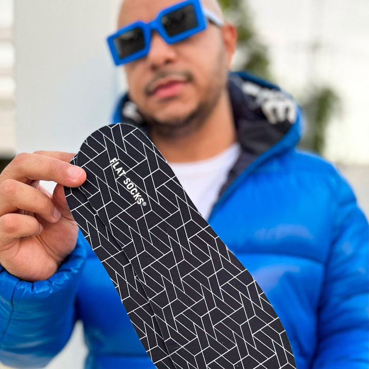 Man wearing blue sunglasses and blue winter coat holding up pair of Black FLAT SOCKS #size_large-up-to-women-s-13-men-s-14