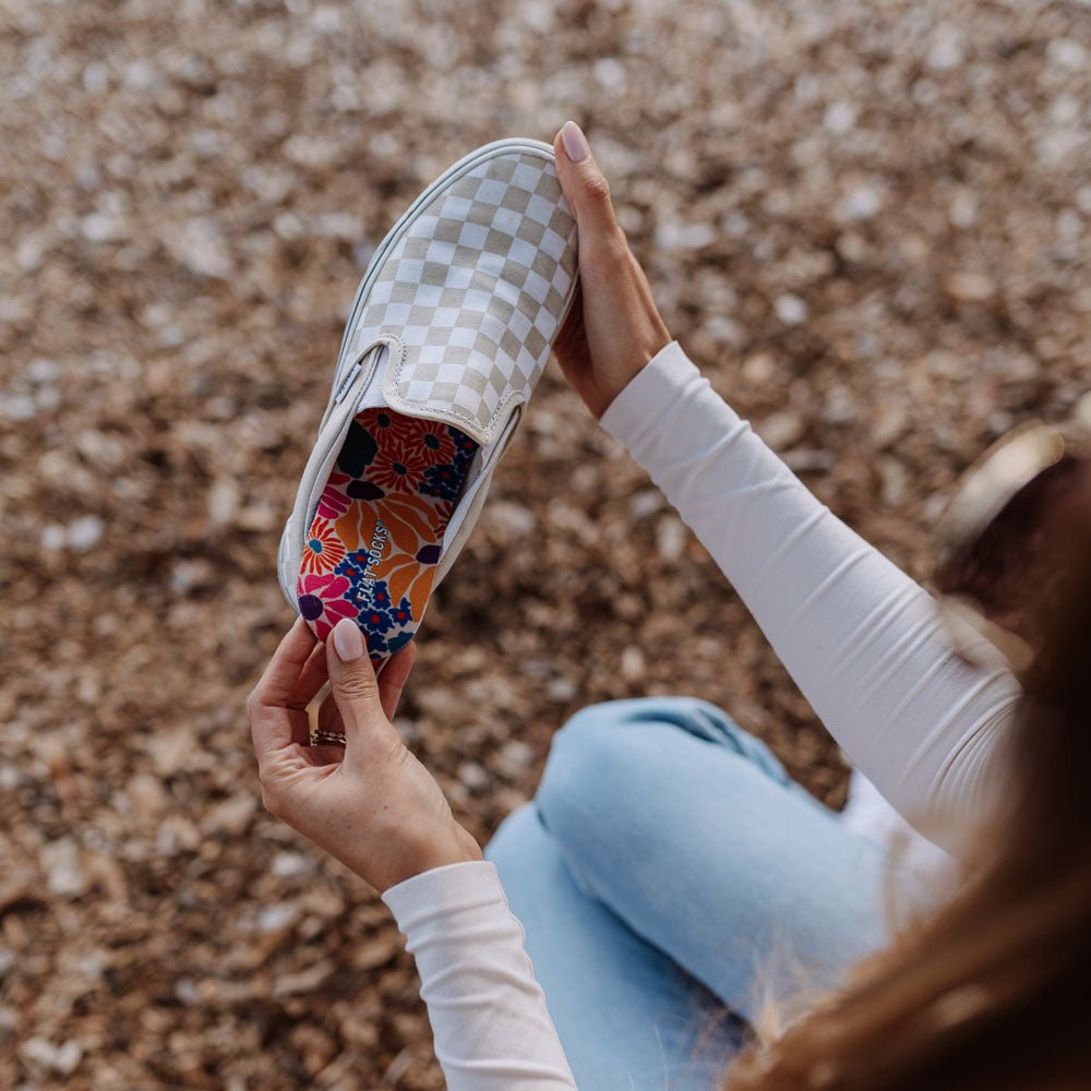 Woman placing Groovy Bloom FLAT SOCKS into white and gray checkered slip-on shoe #size_small-up-to-women-s-11-men-s-10