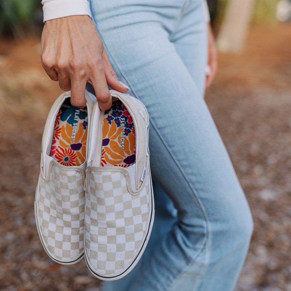 Woman holding pair of white and gray checkered slip-on shoes with Groovy Bloom FLAT SOCKS inside #size_large-up-to-women-s-13-men-s-14