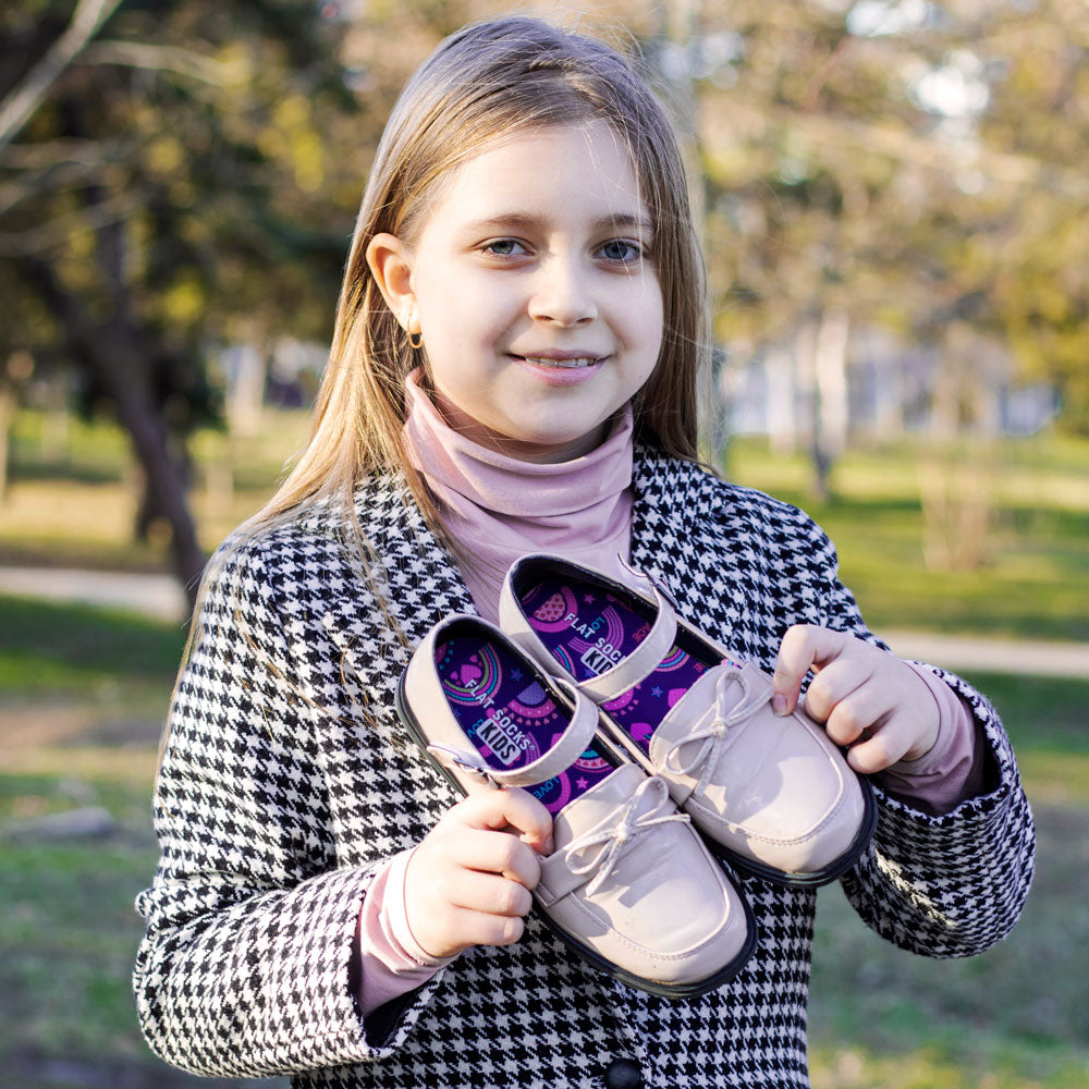 Little girl standing outside at the park while holding up light pink dress shoes with Rainbow Explosion FLAT SOCKS inside #size_8-toddler-to-4-kid-s