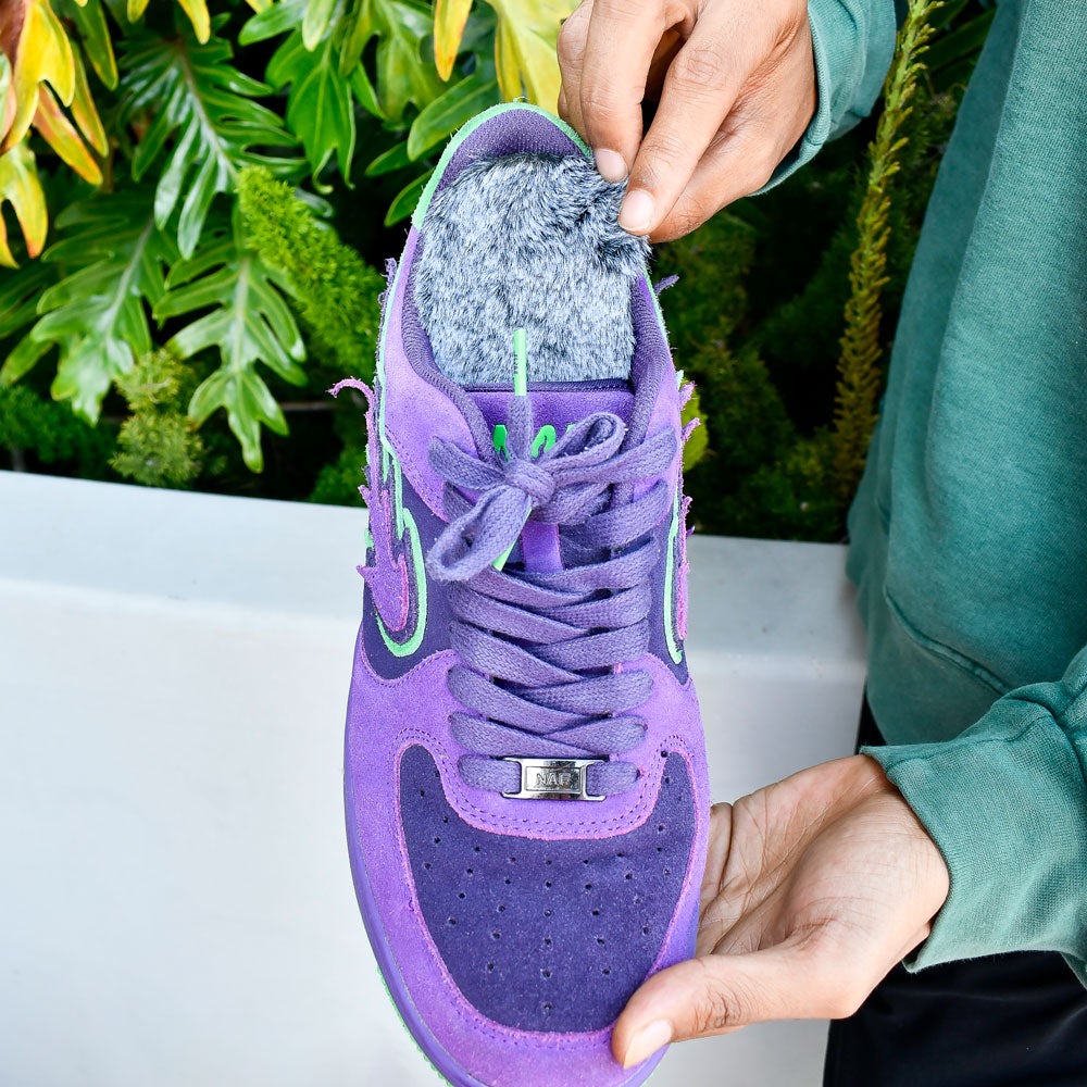 Man standing outside with green plants next to him while holding a pair of purple and green tennis shoes with Koala Faux Fur FLAT SOCKS inside #size_large-up-to-women-s-13-men-s-14