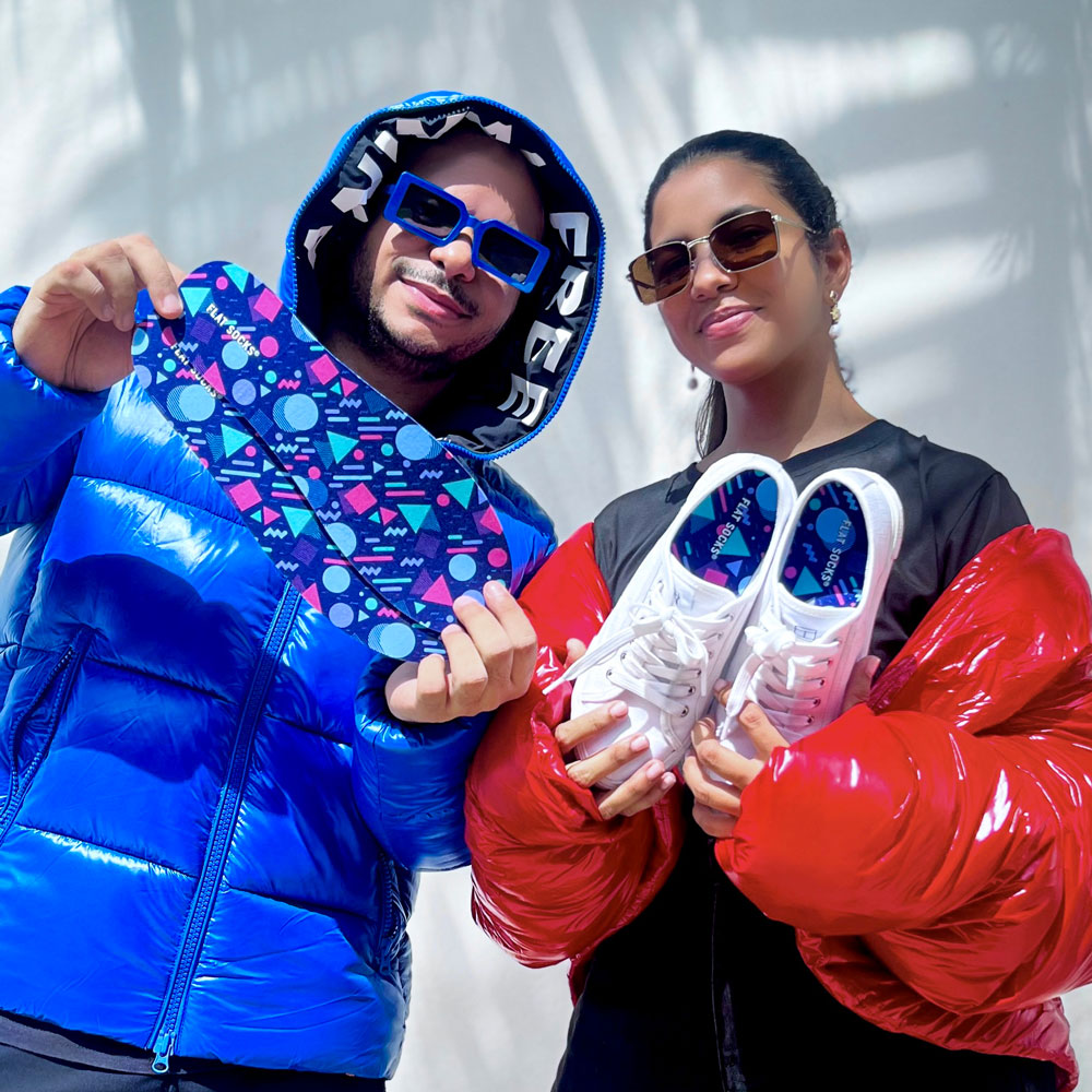 Man wearing shiny blue coat and blue glasses, woman wearing shiny red coat and sunglasses, while holding up Memphis style FLAT SOCKS #size_large-up-to-women-s-13-men-s-14