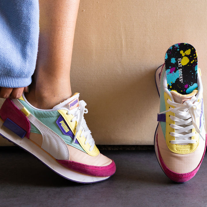 Person placing on a pair of multi-colored Puma shoes with Paint Splatter FLAT SOCKS inside #size_large-up-to-women-s-13-men-s-14