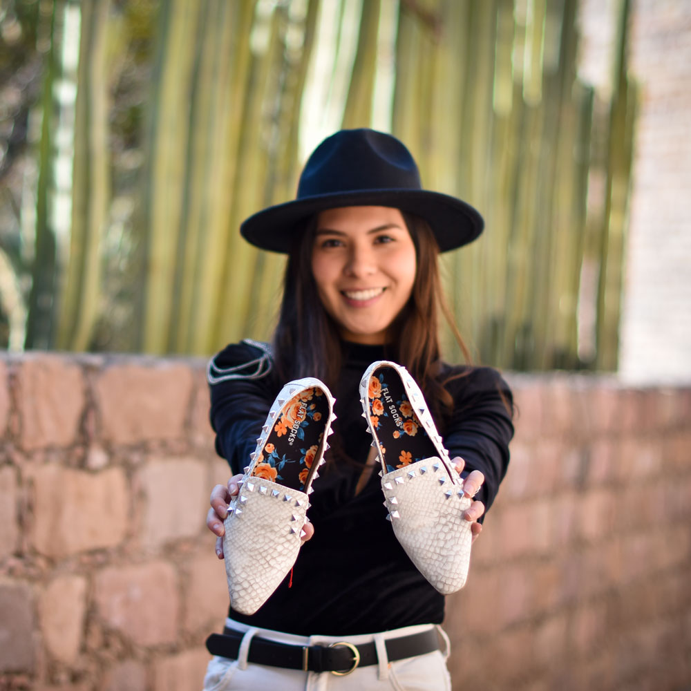 Girl wearing black hat standing outside while holding up a pair of white snake skin flats with Peachy Rose FLAT SOCKS inside #size_small-up-to-women-s-11-men-s-10