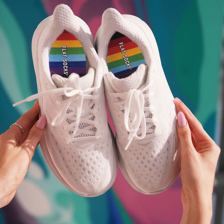 Woman holding up a pair of white sneakers with Rainbow FLAT SOCKS inside #size_large-up-to-women-s-13-men-s-14