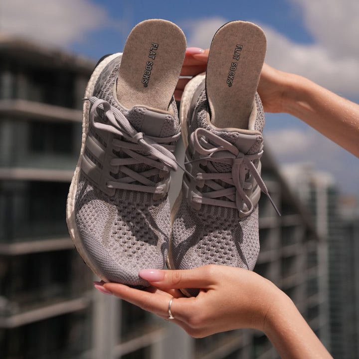 Woman holding up a pair of gray sneakers with Sand FLAT SOCKS inside #size_large-up-to-women-s-13-men-s-14