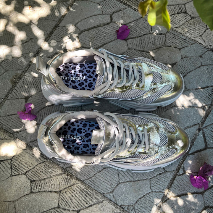 Metallic silver colored sneakers sitting on stone ground with patterns throughout #size_large-up-to-women-s-13-men-s-14