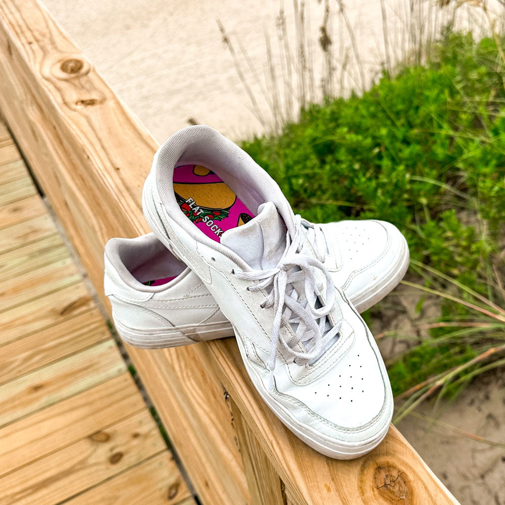 Pair of white sneakers sitting on pier at the beach with pink taco FLAT SOCKS inside #size_small-up-to-women-s-11-men-s-10