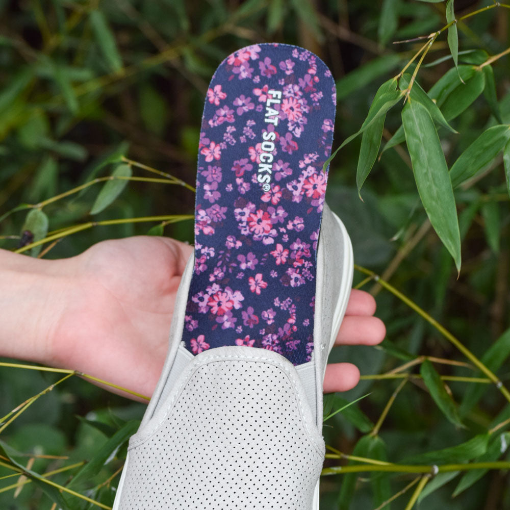 Person holding gray slip-on flat shoe with Violet Thatcher FLAT SOCKS inside, green plant in background #size_small-up-to-women-s-11-men-s-10